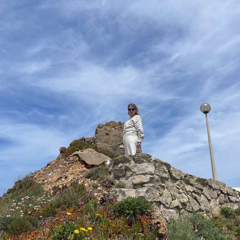 Becca standing on the rocky coast beneath a wide blue sky